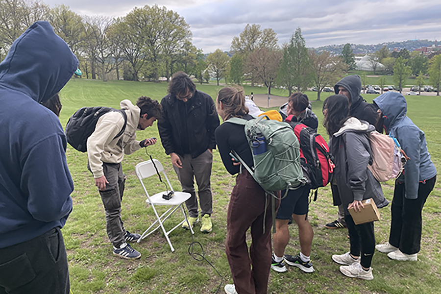 Group of students on a grassy hill looking at a ham radio